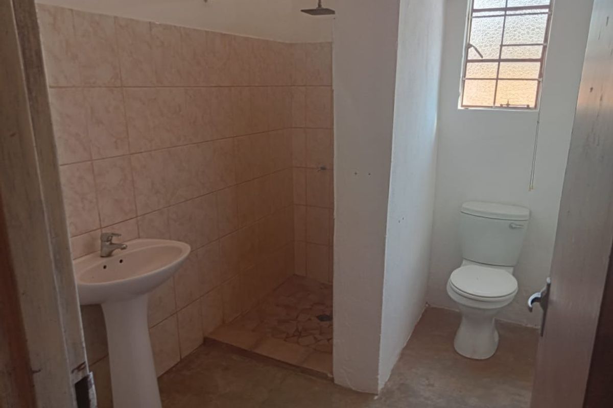 A functional bathroom featuring a pedestal basin, shower enclosure, and toilet, with tiled wall finishes and a steel-framed window.