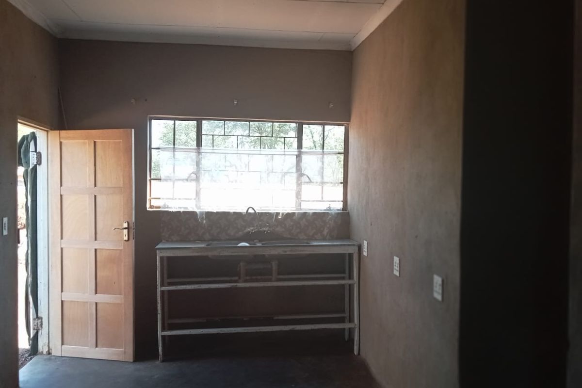 A basic, unfinished kitchen area featuring a simple sink unit, tiled splashback, and raw plaster walls, offering a blank canvas for renovation.