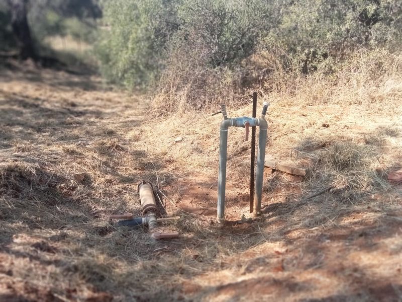 Outdoor utility area featuring exposed borehole pump infrastructure and irrigation piping set within a natural farm landscape.