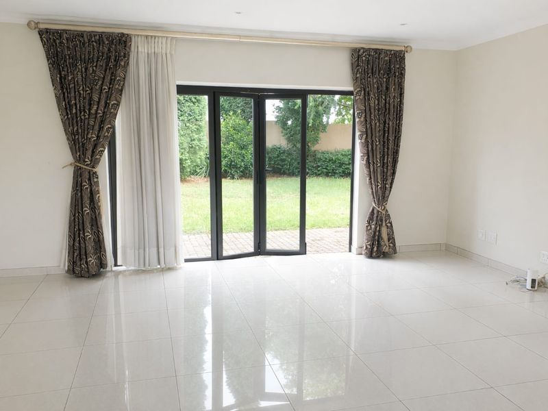 A bright, empty living room featuring polished tiled floors and modern bi-fold doors that open directly onto the rear garden.