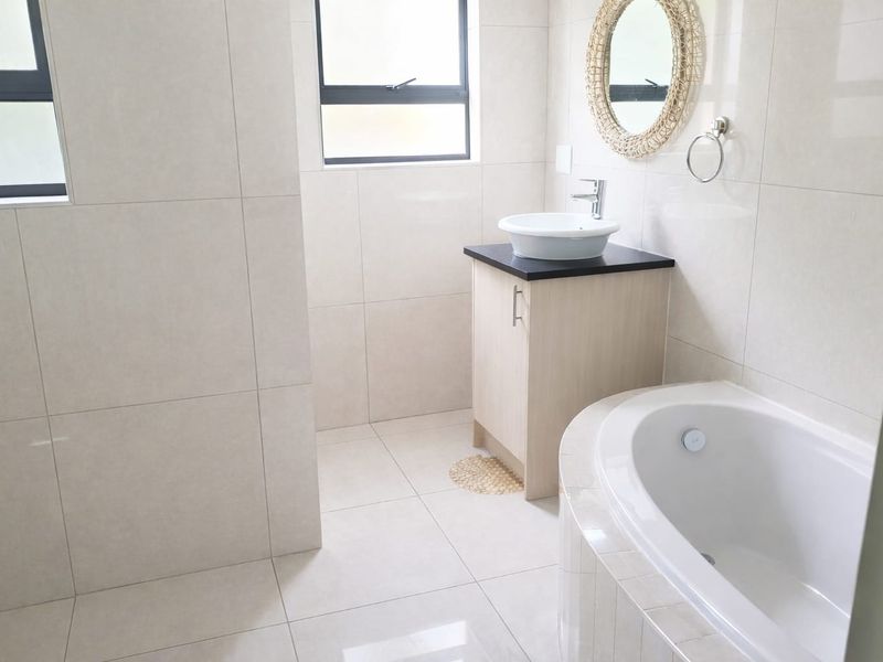 Modern bathroom featuring a built-in vanity with vessel sink, tiled finishes throughout, and a built-in bathtub.
