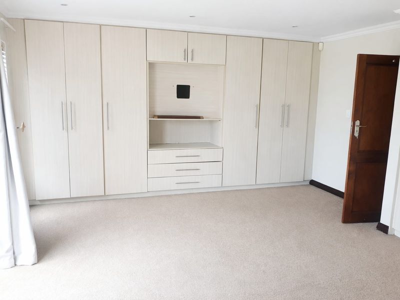 A spacious, empty bedroom featuring extensive built-in cabinetry with integrated shelving and drawers, neutral carpeting, and recessed ceiling lighting.