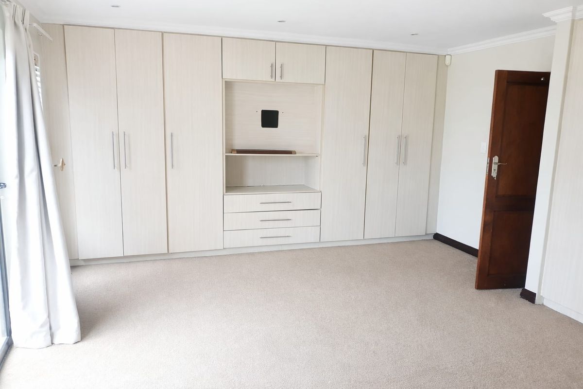 A spacious, empty bedroom featuring extensive built-in cabinetry with integrated shelving and drawers, neutral carpeting, and recessed ceiling lighting.