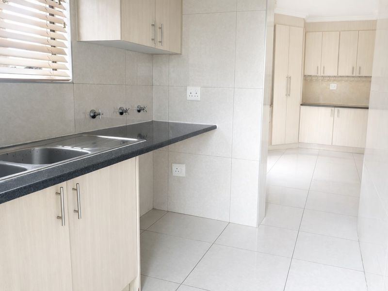 A clean, modern kitchen featuring light wood cabinetry, granite countertops, tiled flooring, and a double sink with ample storage space.