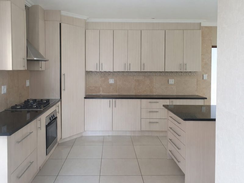A clean, modern kitchen featuring light wood-finish cabinetry, dark granite countertops, a gas hob, built-in oven, and a functional central island.