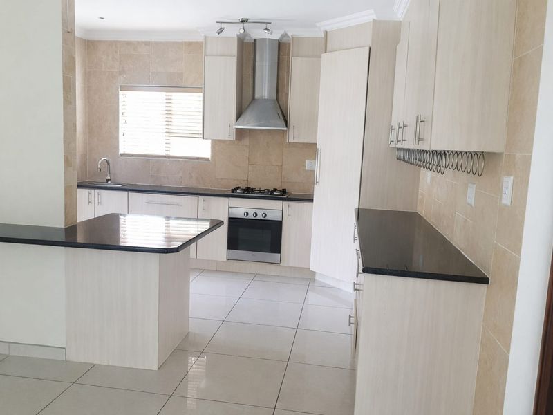 Modern kitchen featuring light wood cabinetry, dark granite countertops, stainless steel appliances, and neutral tiled flooring throughout.