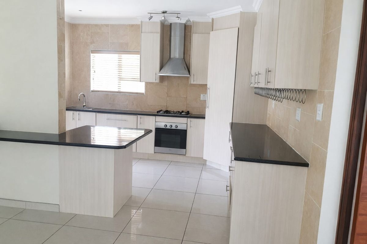 Modern kitchen featuring light wood cabinetry, dark granite countertops, stainless steel appliances, and neutral tiled flooring throughout.