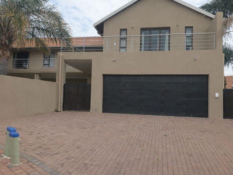 Front elevation of a double-story house featuring a paved driveway, large garage door, and an upper-level balcony with stainless steel railings.