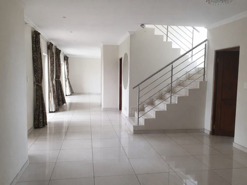 Spacious open-plan living area featuring neutral tiled flooring, a modern staircase with stainless steel railings, and abundant natural light.