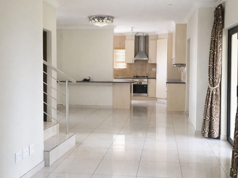 Spacious open-plan living and kitchen area featuring neutral tiled flooring, modern cabinetry, built-in appliances, and direct access to an outdoor space.