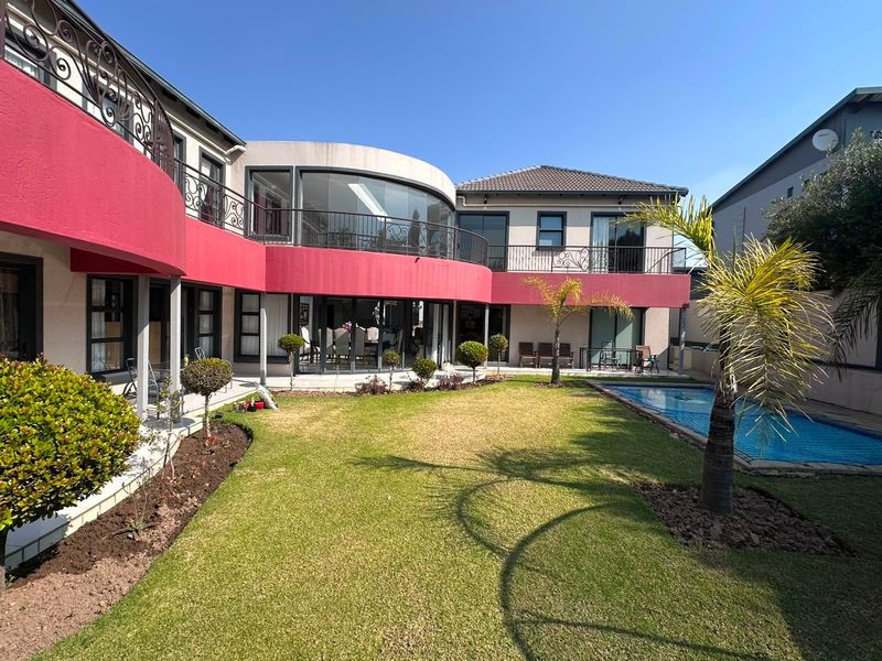 Rear view of a two-story house featuring a curved architectural design, upper-level balcony with wrought iron railings, swimming pool, and a landscaped garden.