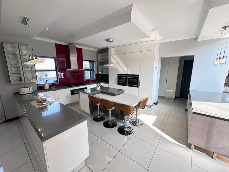 Modern kitchen featuring high-gloss cabinetry, stone countertops, a central island with breakfast bar, integrated double ovens, and sleek tiled flooring.