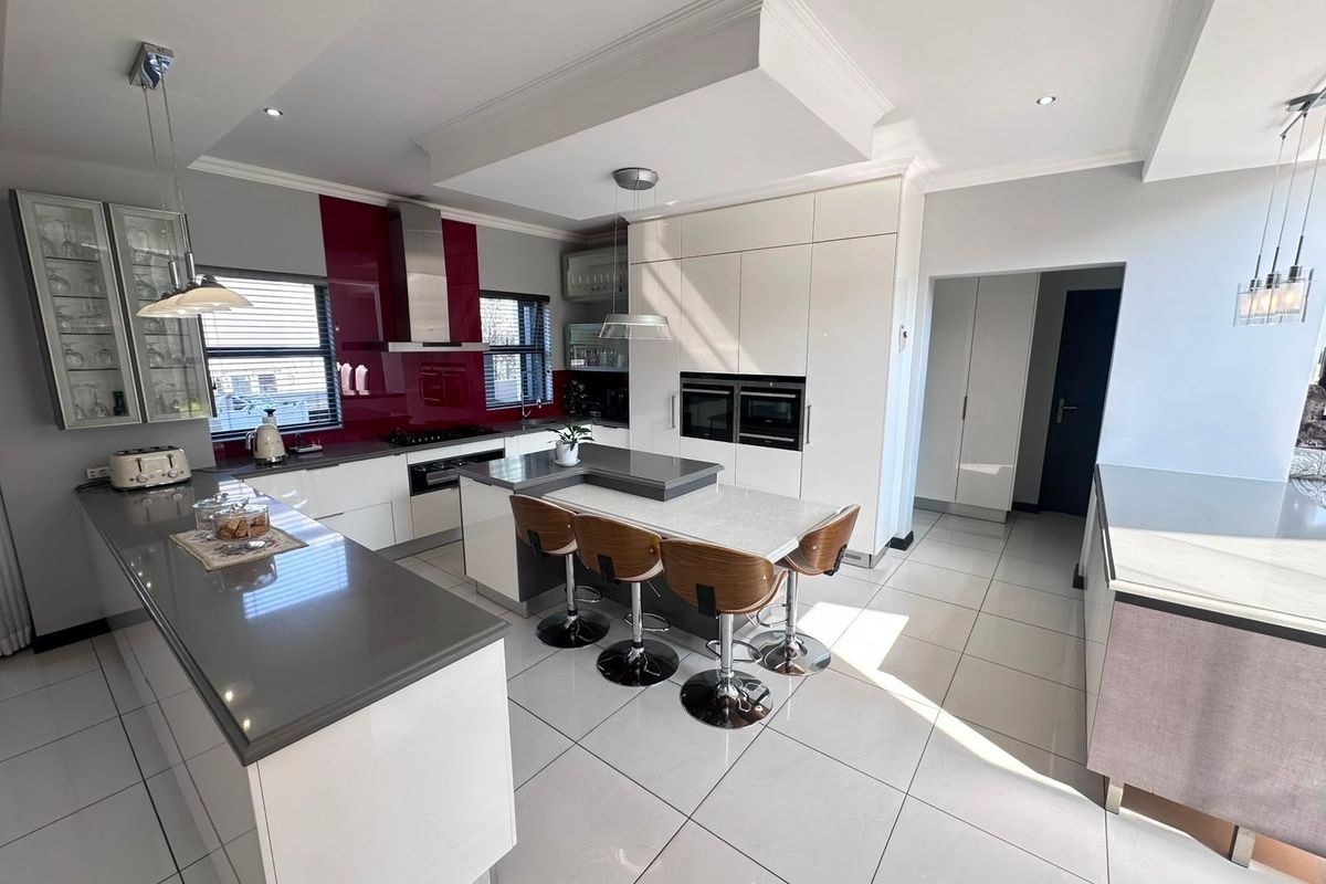 Modern kitchen featuring high-gloss cabinetry, stone countertops, a central island with breakfast bar, integrated double ovens, and sleek tiled flooring.