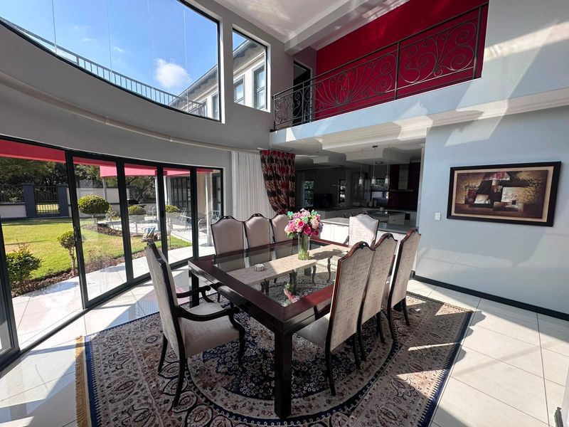 Spacious open-plan dining area featuring double-volume ceilings, large glass sliding doors opening to the garden, and a mezzanine level with decorative wrought iron railing.