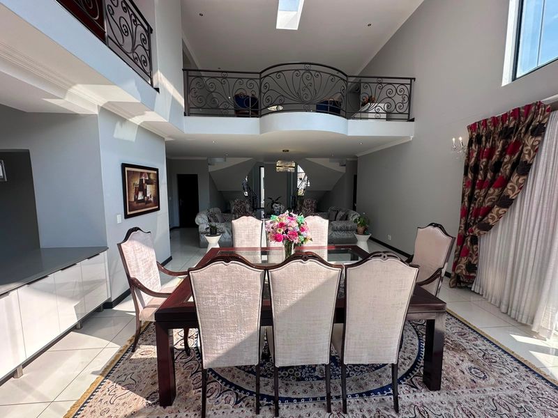 Spacious open-plan dining area featuring a double-volume ceiling, mezzanine level with decorative wrought iron railing, skylight, and modern tiled flooring.