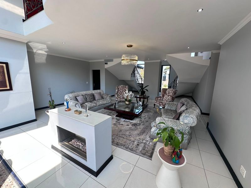 Spacious living room featuring a modern double-sided fireplace, tiled flooring, recessed lighting, and an elegant staircase with a wrought iron balustrade.
