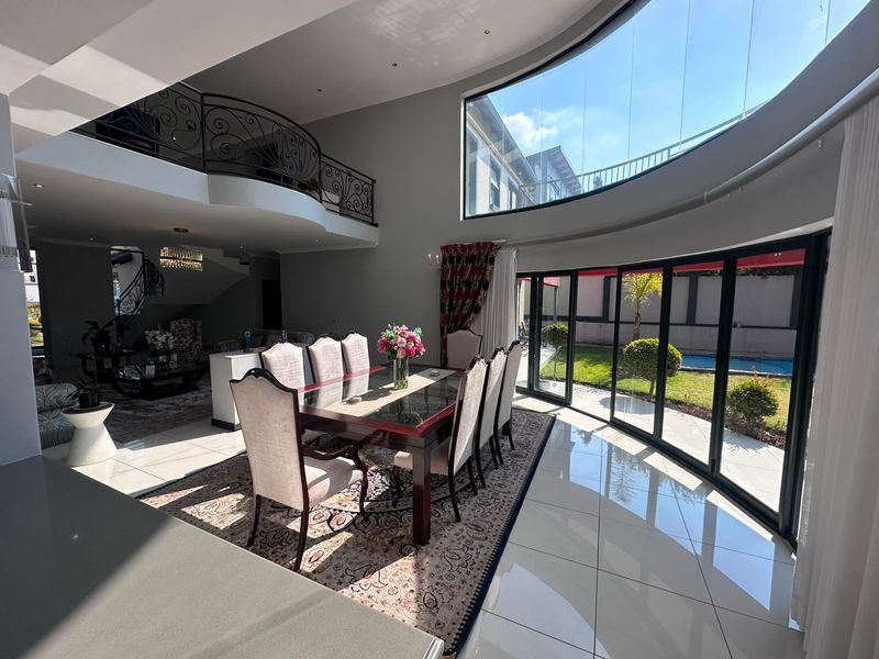 Spacious open-plan dining area featuring high ceilings, a mezzanine level with wrought iron railings, and expansive curved glass walls overlooking the garden.