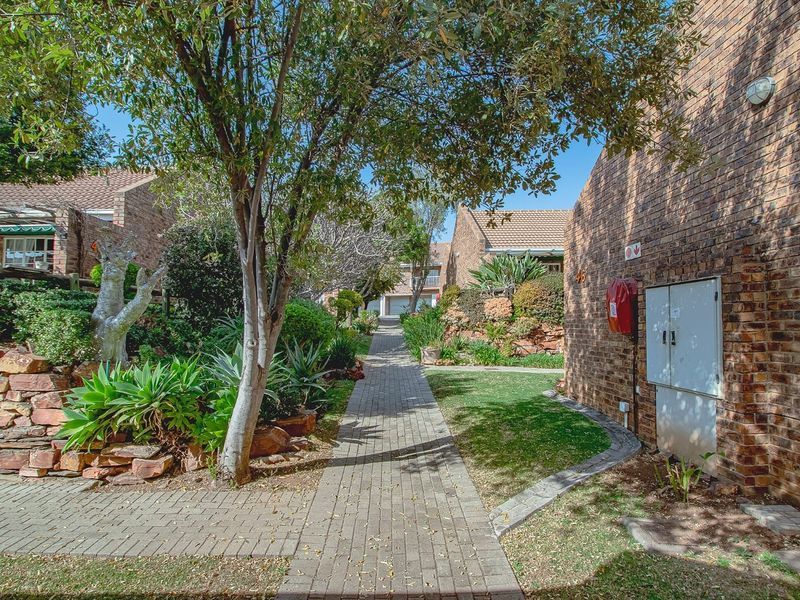 A view of the paved walkway leading through the townhouse complex, featuring established landscaping, brick facades, and communal exterior infrastructure.