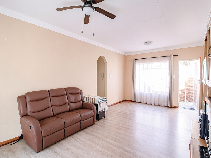 A bright living room featuring laminate flooring, a ceiling fan, and an arched doorway leading to other areas of the townhouse.