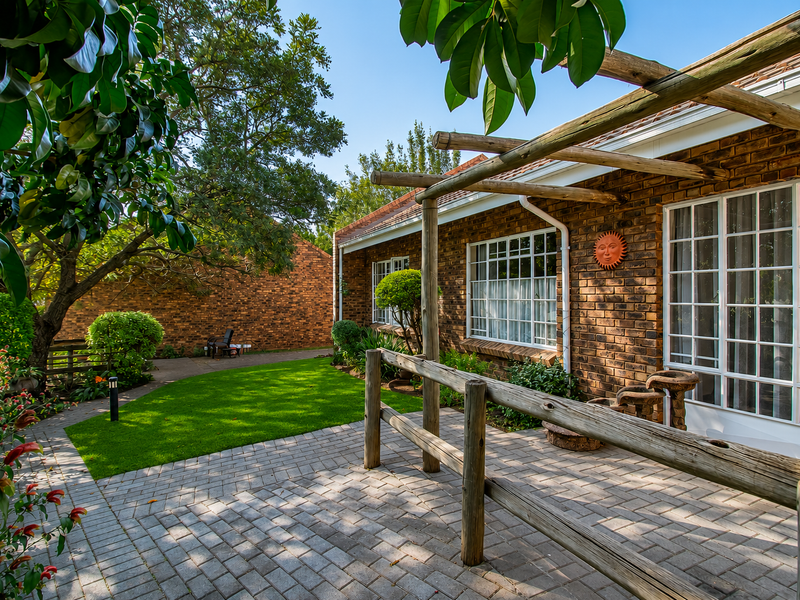 A well-maintained rear exterior featuring a brick facade, a timber pergola over a paved patio area, and a landscaped garden with mature trees.