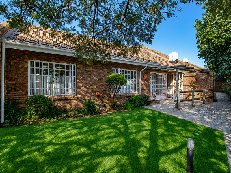 A well-maintained townhouse exterior featuring a face brick facade, tiled roof, paved walkway, and a charming timber pergola over the entrance area.