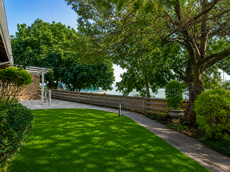 A well-maintained garden area featuring a manicured lawn, brick paved pathway, timber fencing, and a pergola structure.