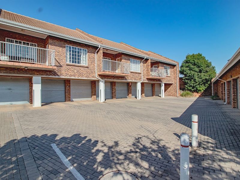 Exterior view of a townhouse complex featuring a paved driveway, multiple roller garage doors, and upper-level balconies with metal railings.