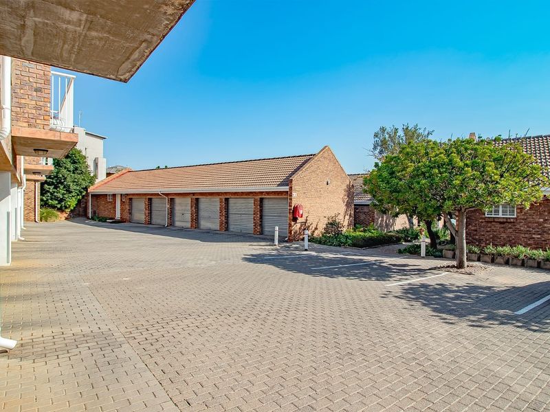 A view of the townhouse complex exterior featuring a paved driveway, multiple garage units, and established brickwork architecture.