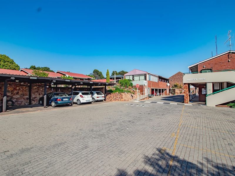 Exterior view of the townhouse complex entrance featuring paved parking areas, covered carports, and brick building facades.