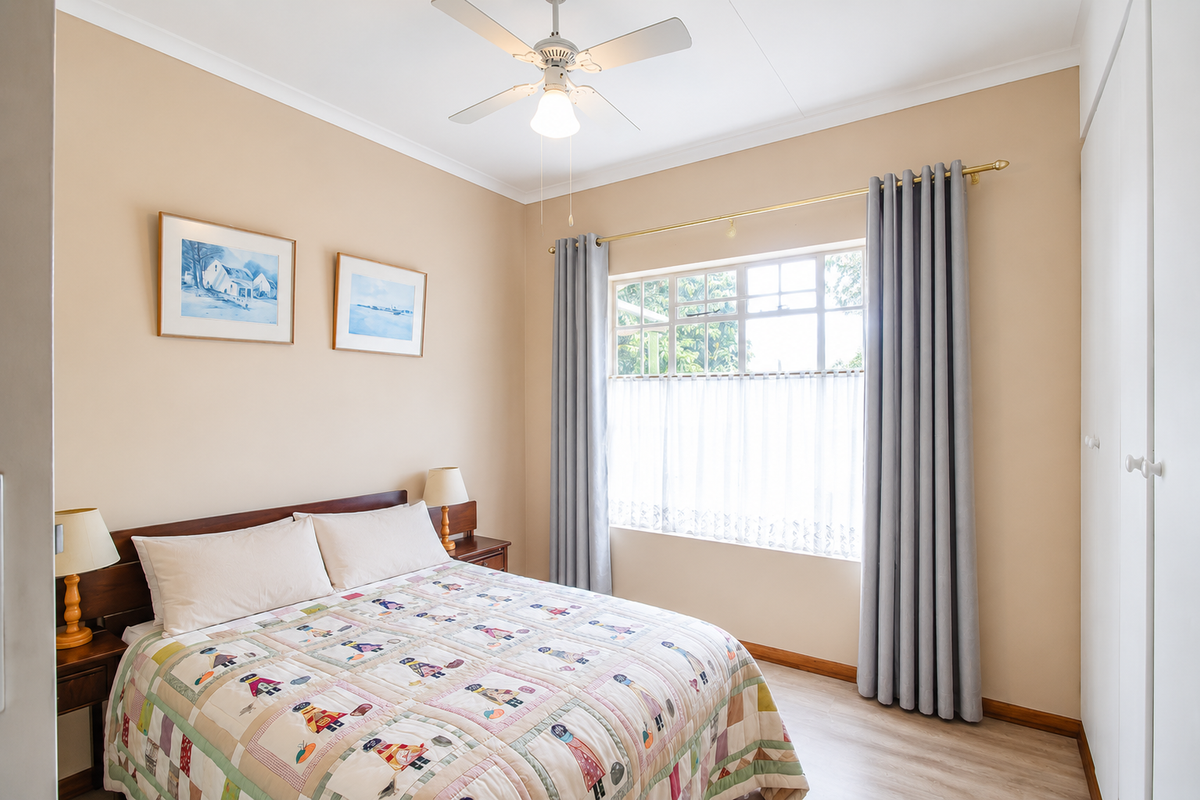 A well-maintained bedroom featuring laminate flooring, built-in cupboards, a ceiling fan, and a large multi-pane window allowing for natural light.