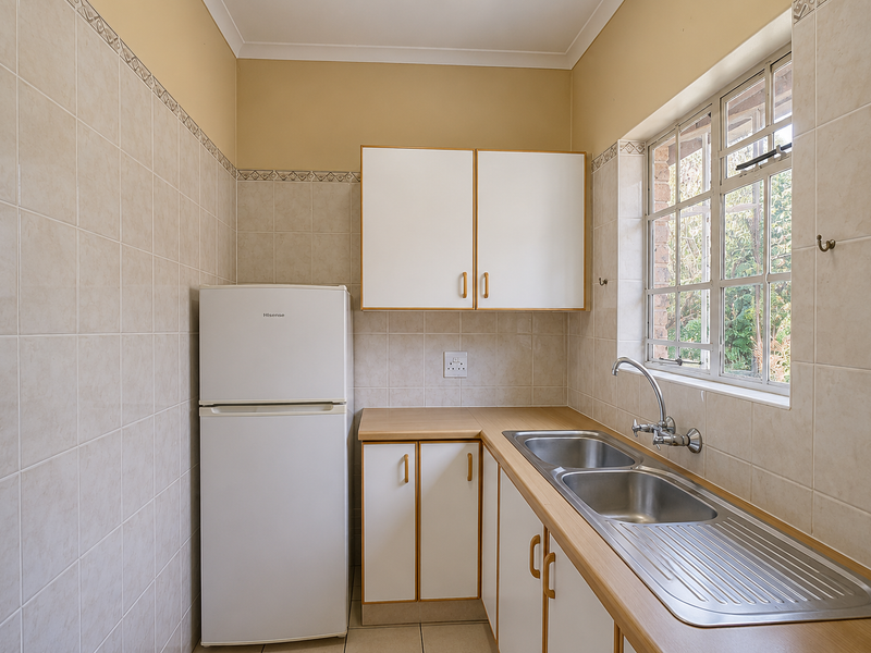 A functional scullery featuring tiled walls, built-in cabinetry, a double bowl stainless steel sink, and a window with security bars.