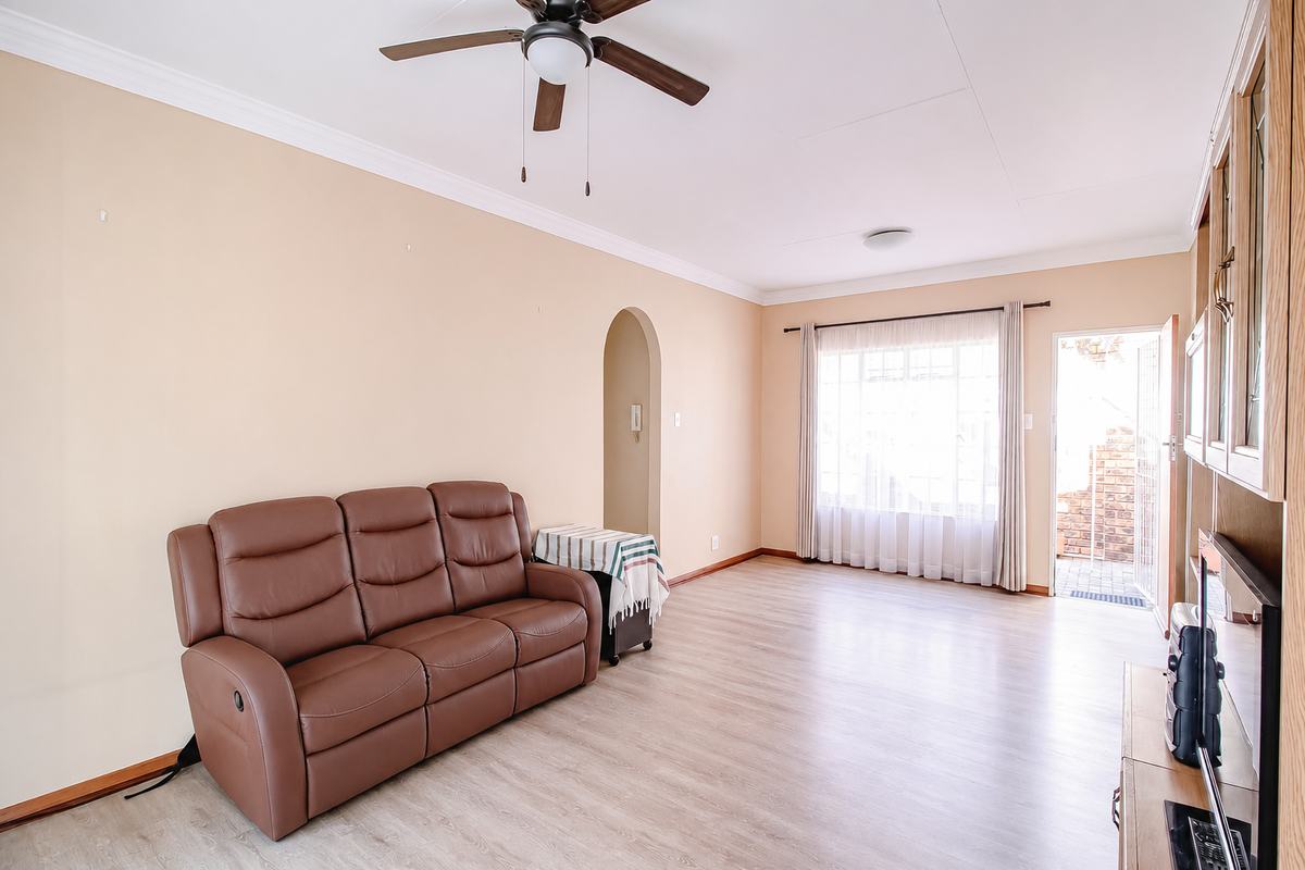 A bright living room featuring laminate flooring, a ceiling fan, and an arched doorway leading to adjacent spaces, with direct access to an outdoor area.