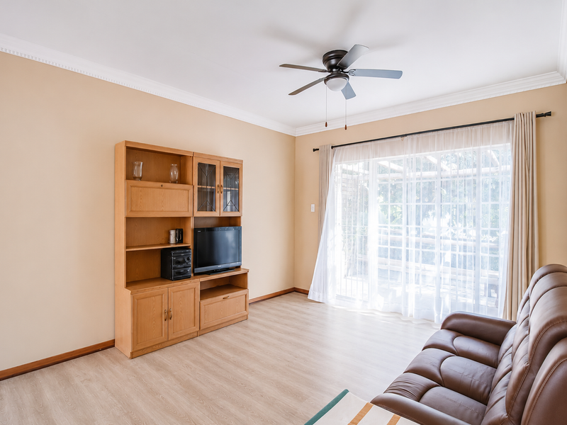 A bright living room featuring laminate flooring, crown molding, a ceiling fan, and a large sliding glass door providing access to the outdoor area.