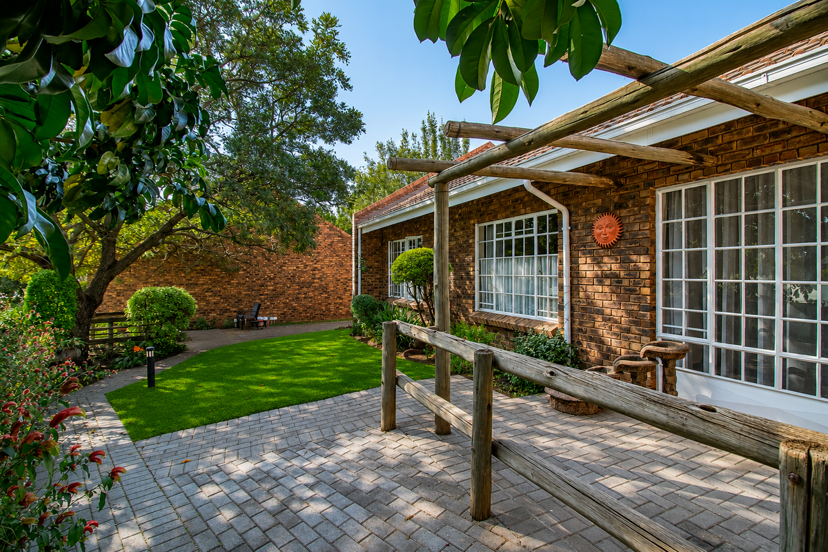 A well-maintained rear exterior featuring a brick facade, a paved patio area with a timber pergola, and a landscaped garden.