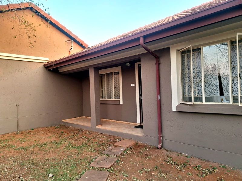 Rear view of the townhouse featuring a covered patio, tiled roof, and a small garden area with concrete stepping stones.