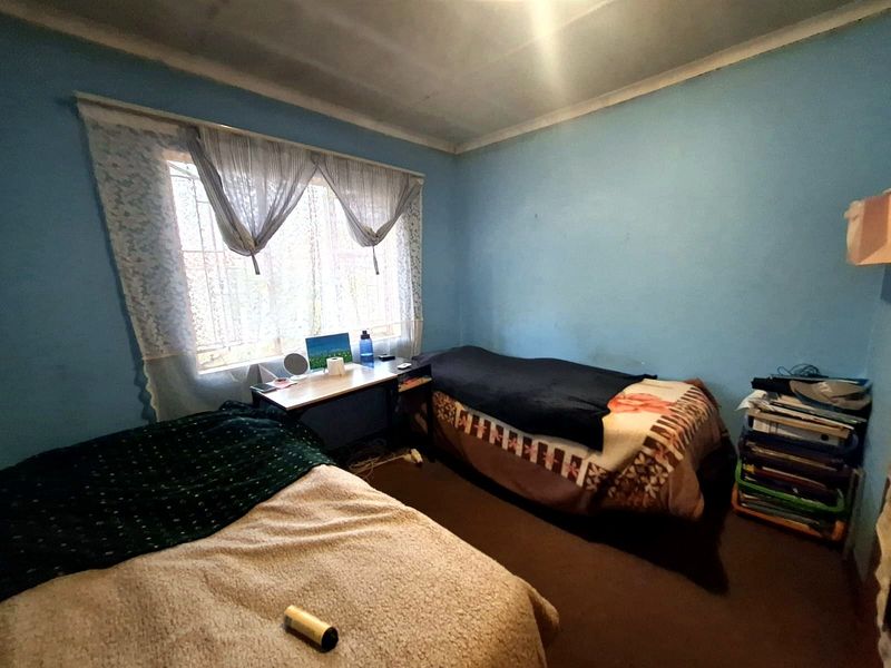 A bedroom featuring blue walls, a window with security bars, and a ceiling with visible staining, requiring cosmetic updates to improve its overall condition.