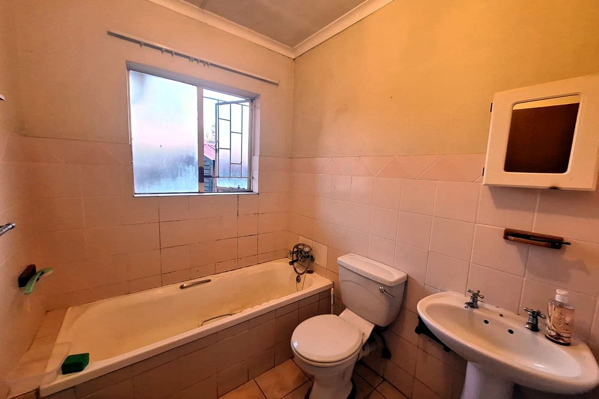 A dated bathroom featuring a standard bathtub, pedestal basin, and toilet with tiled finishes, requiring cosmetic updates to improve its overall condition.