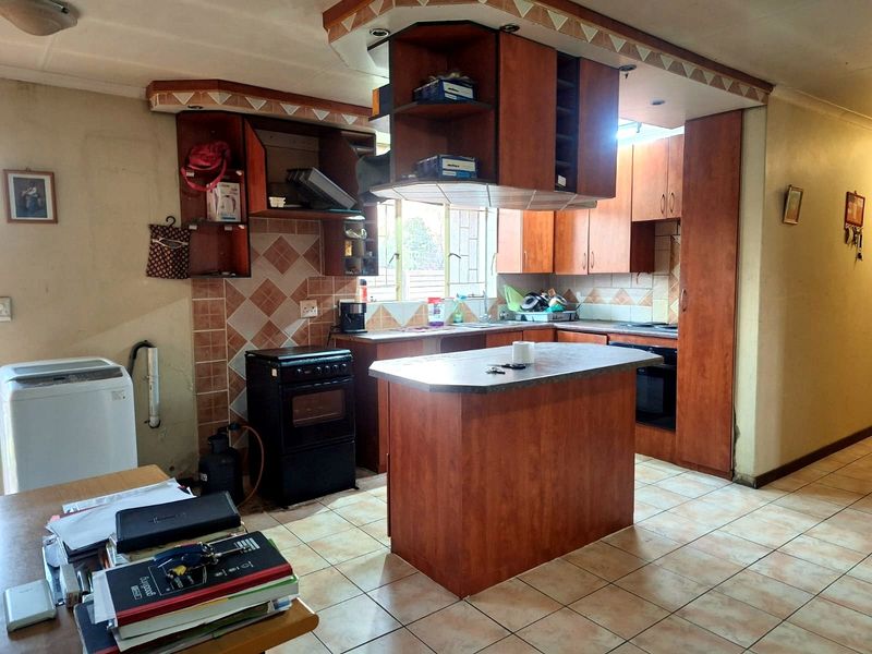 A dated kitchen featuring wooden cabinetry, a central island, tiled flooring, and a tiled backsplash, offering potential for a modern renovation.
