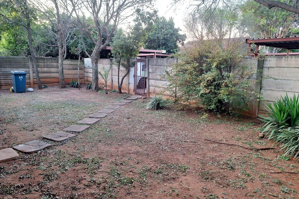 A private rear garden area featuring a precast concrete boundary wall, a metal pedestrian gate, and a stone paver pathway leading across the yard.