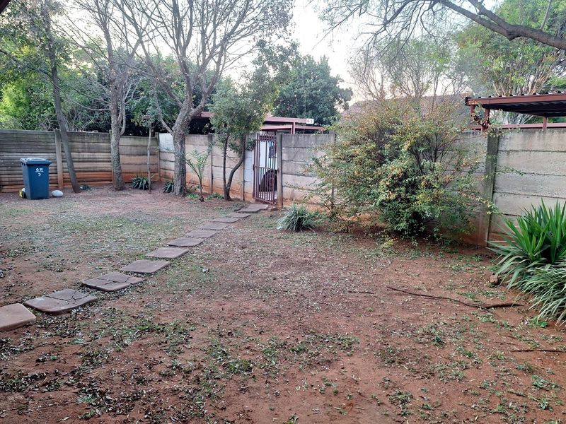 A private rear garden area featuring a precast concrete boundary wall, a metal pedestrian gate, and a stone paver pathway leading across the yard.