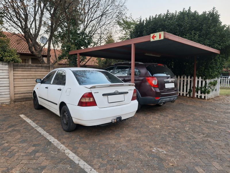 Covered carport parking area with paved driveway and secure boundary fencing.