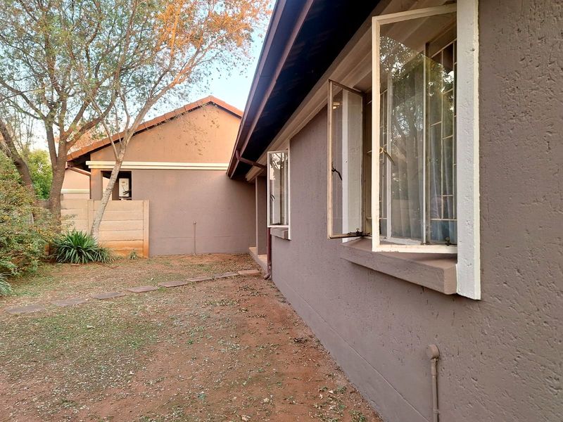 A view of the rear exterior of the townhouse, featuring a private garden area, boundary wall, and casement windows with security bars.