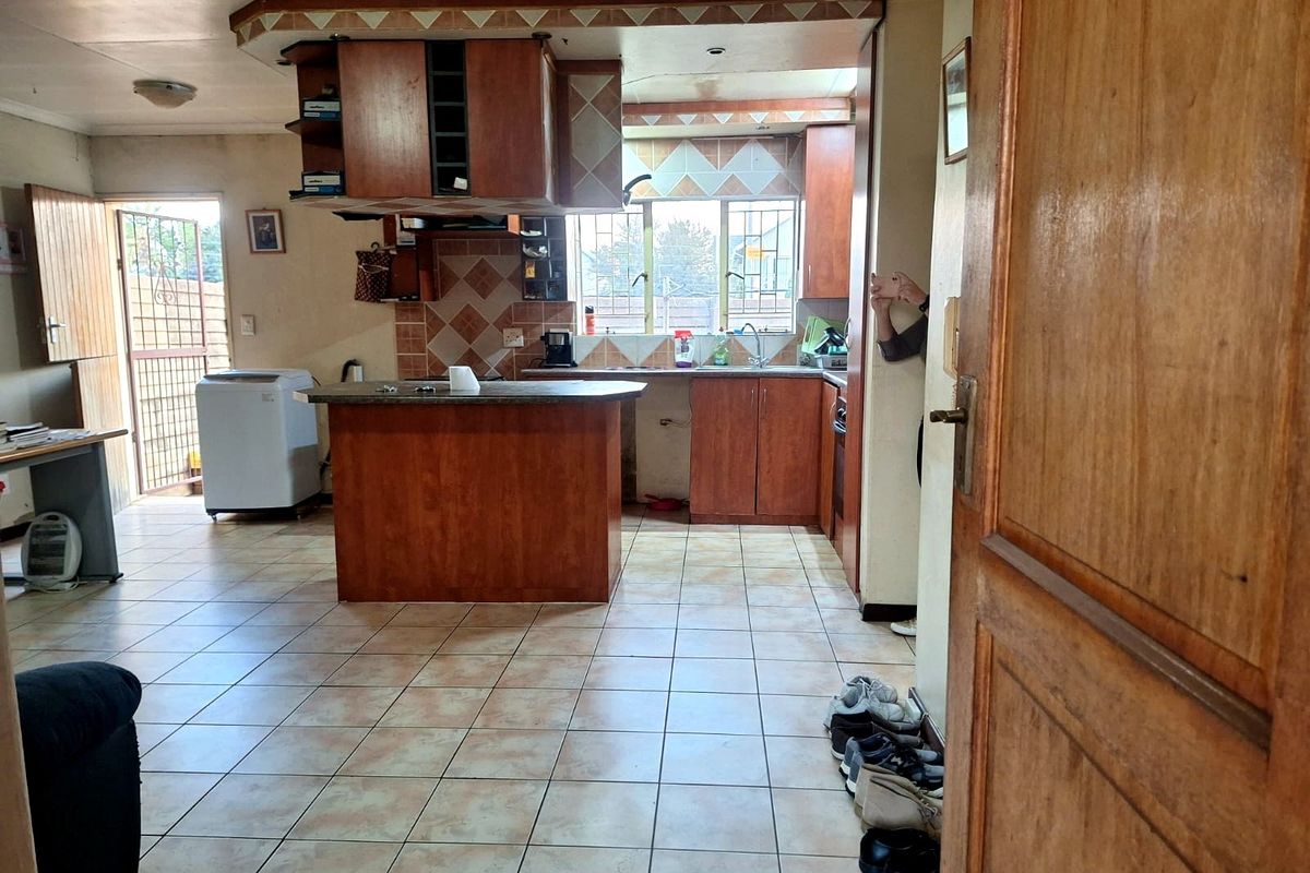 A dated kitchen featuring wooden cabinetry, a central island, tiled flooring, and a tiled backsplash, with direct access to an exterior security gate.