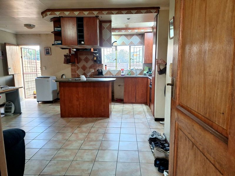 A dated kitchen featuring wooden cabinetry, a central island, tiled flooring, and a tiled backsplash, with direct access to an exterior security gate.