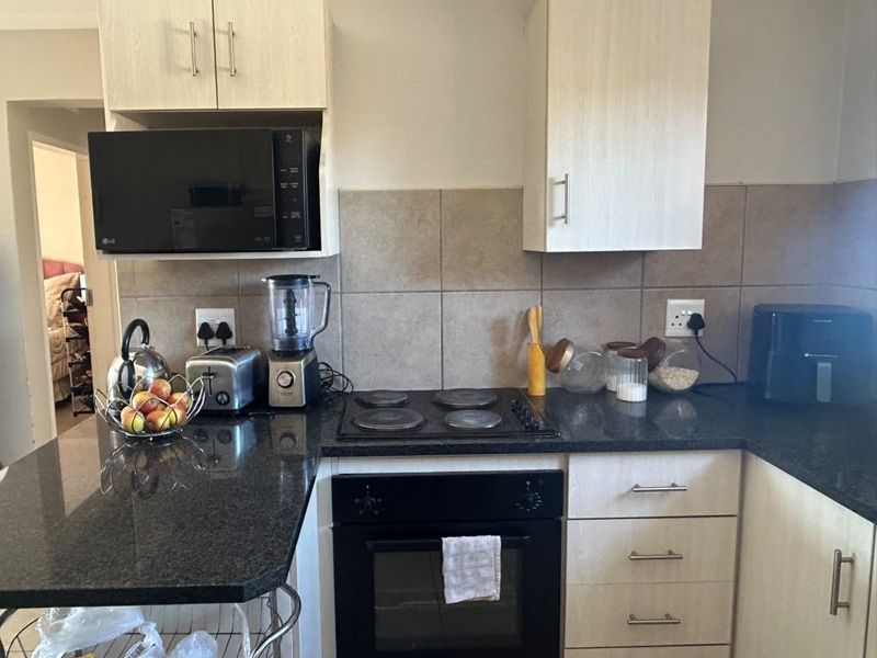 A functional kitchen featuring granite countertops, built-in oven, electric hob, and light-toned cabinetry with a tiled backsplash.