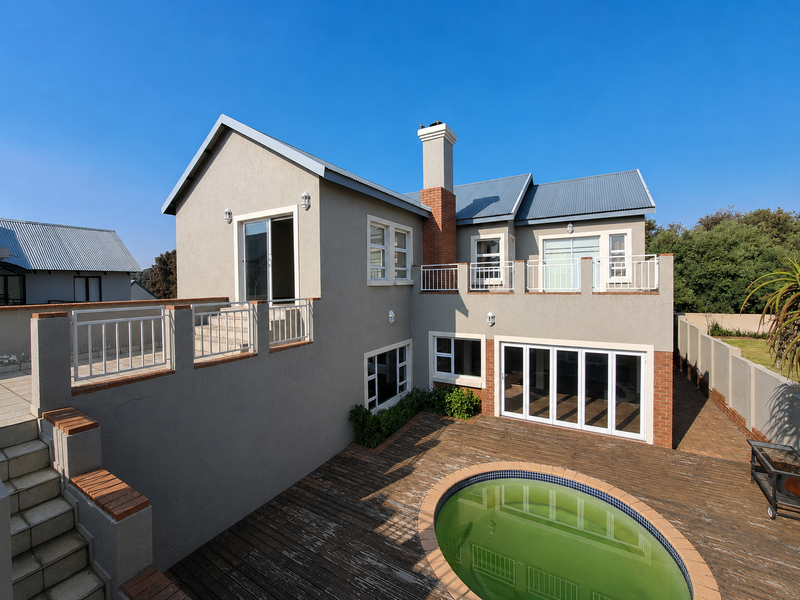 Rear view of a multi-level house featuring a swimming pool, timber decking, brick chimney, and balcony access through sliding doors.