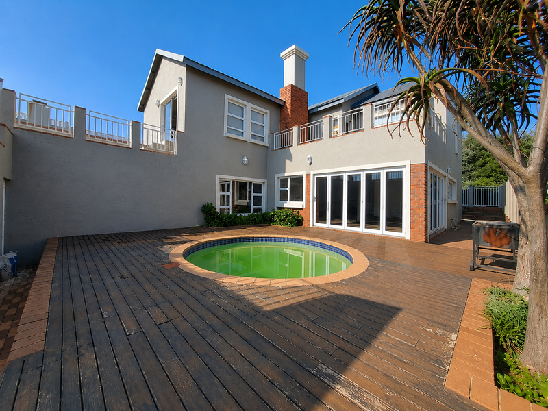 Rear exterior view featuring a circular swimming pool set within a timber deck, adjacent to a two-story home with folding glass doors.