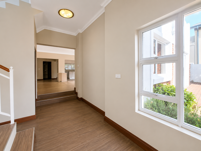 A bright and spacious entrance hallway featuring modern tiled flooring, clean neutral walls, and a staircase leading to upper levels.
