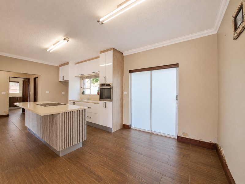 Modern kitchen featuring a central island with integrated hob, built-in oven, and sliding door access to the exterior, finished with tiled flooring.