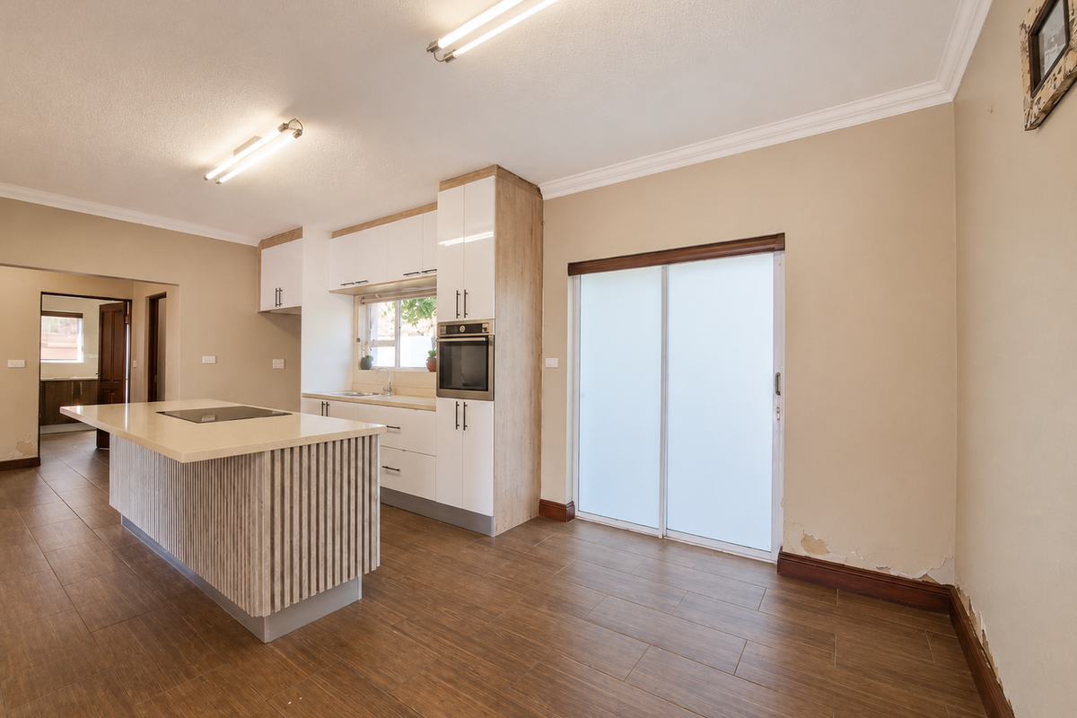 Modern kitchen featuring a central island with integrated hob, built-in oven, and sliding door access to the exterior, finished with tiled flooring.